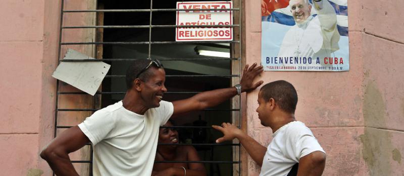 Tres personas conversan junto a un cartel alusivo a la visita del Papa Francisco. Foto: EFE