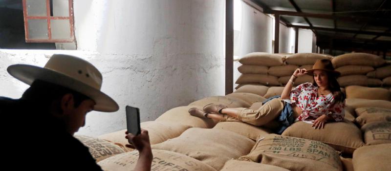 Visitantes toman fotos sobre unos sacos con granos de café durante una excursión para turistas a una finca, en el municipio de Pastores, departamento de Sacatepéquez, en Guatemala. Foto: EFE