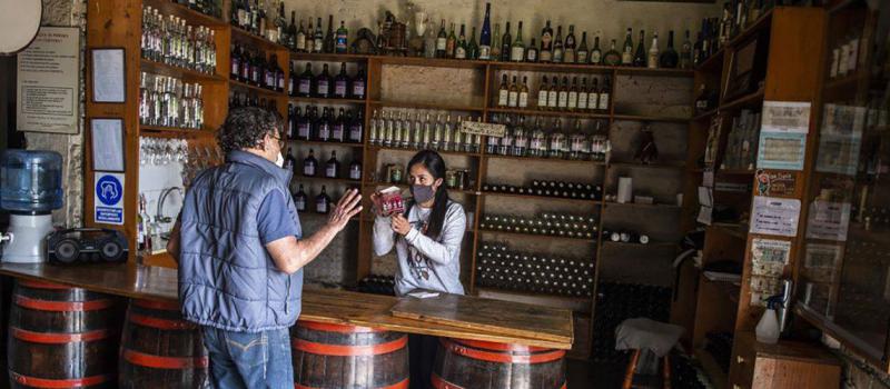 Una empleada atiende a un cliente en la recepción de la destilería Ugarelli, en Lima. Los productores de esta bebida se quejan de las millonarias pérdidas que deja la pandemia al sector. Foto: Ernesto Benavides / AFP